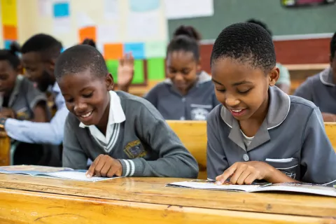 smiling girls reading from books on their desks in class.