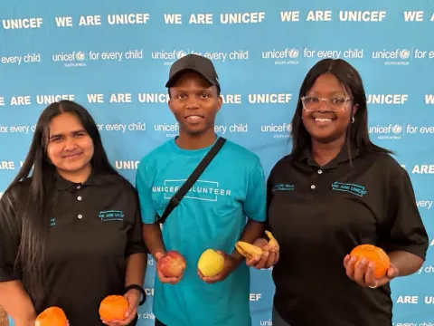 Three UNICEF volunteers holding fresh fruit