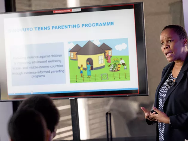 A woman standing next a screen with a presentation on parenting on it.