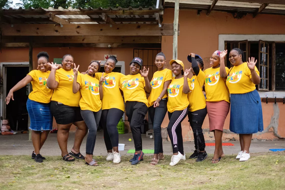 A group of women wearing yellow Power of Play t-shirts gather happily for a photo.