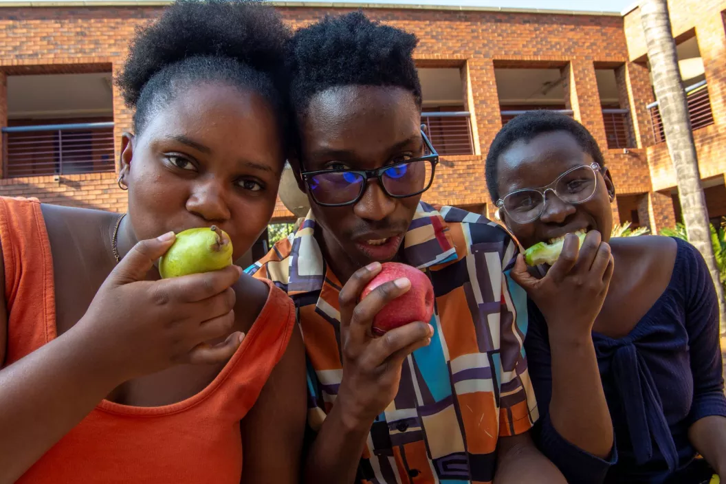 Three young people smiling broadly while eating apples
