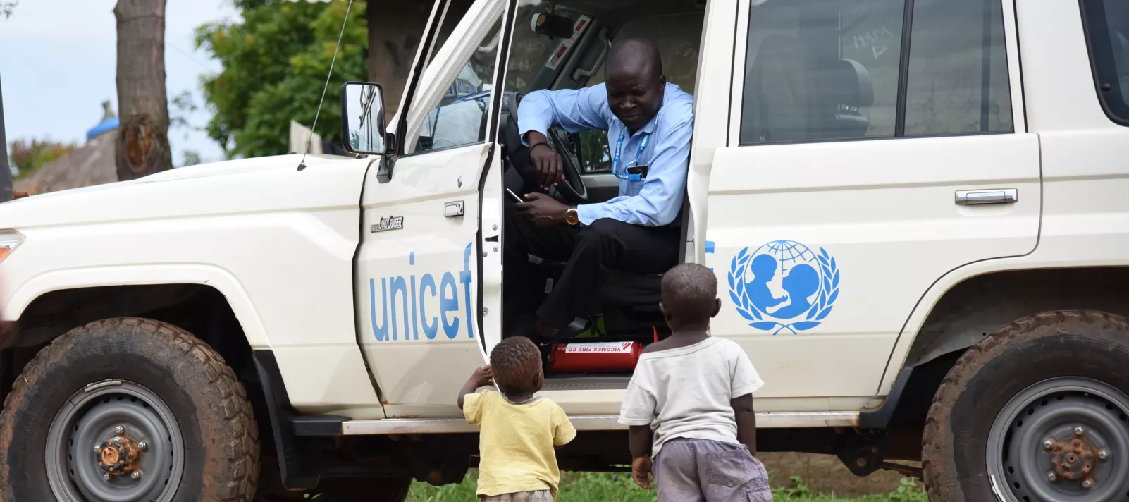 To children are approaching a UNICEF car and driver