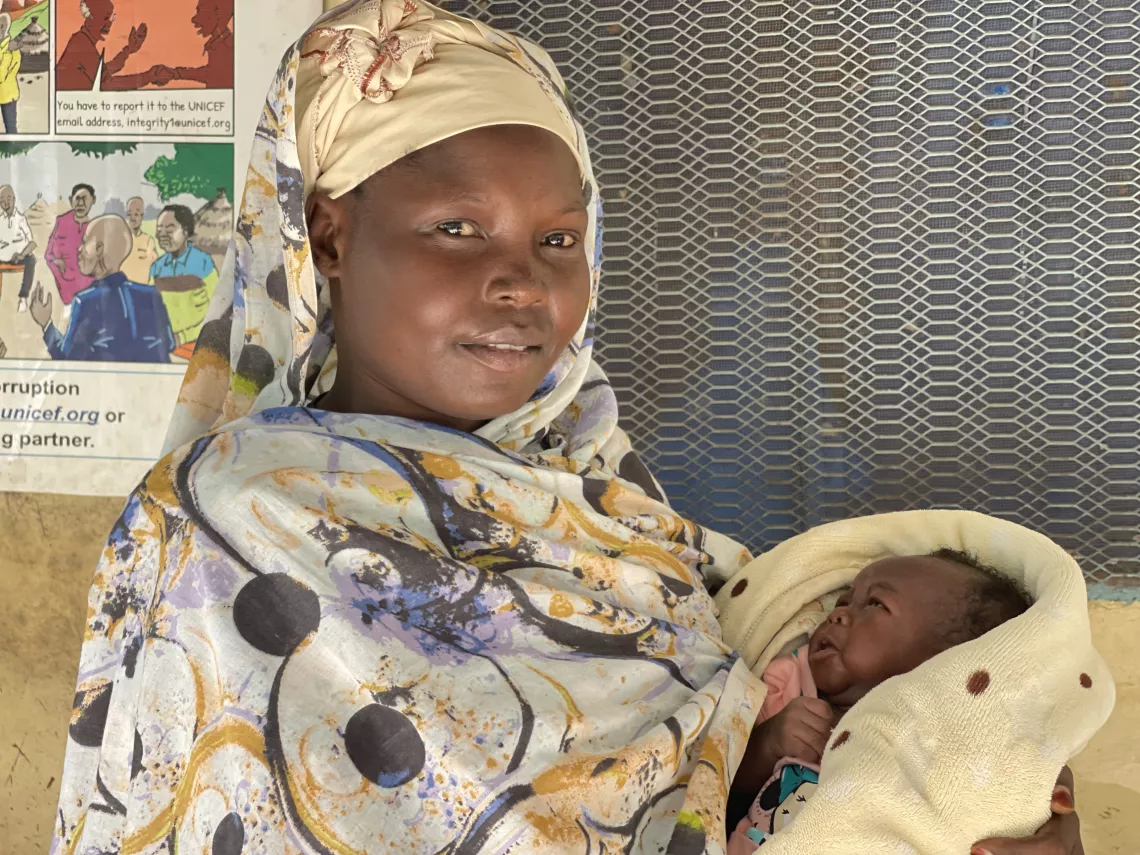 Roda Daniel excited while holding her newborn following the vaccination at Bunj PHCC