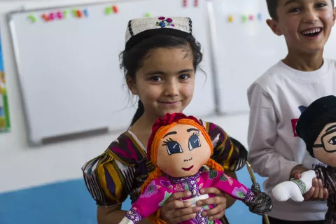 A smiling girl holding a doll in her hands 