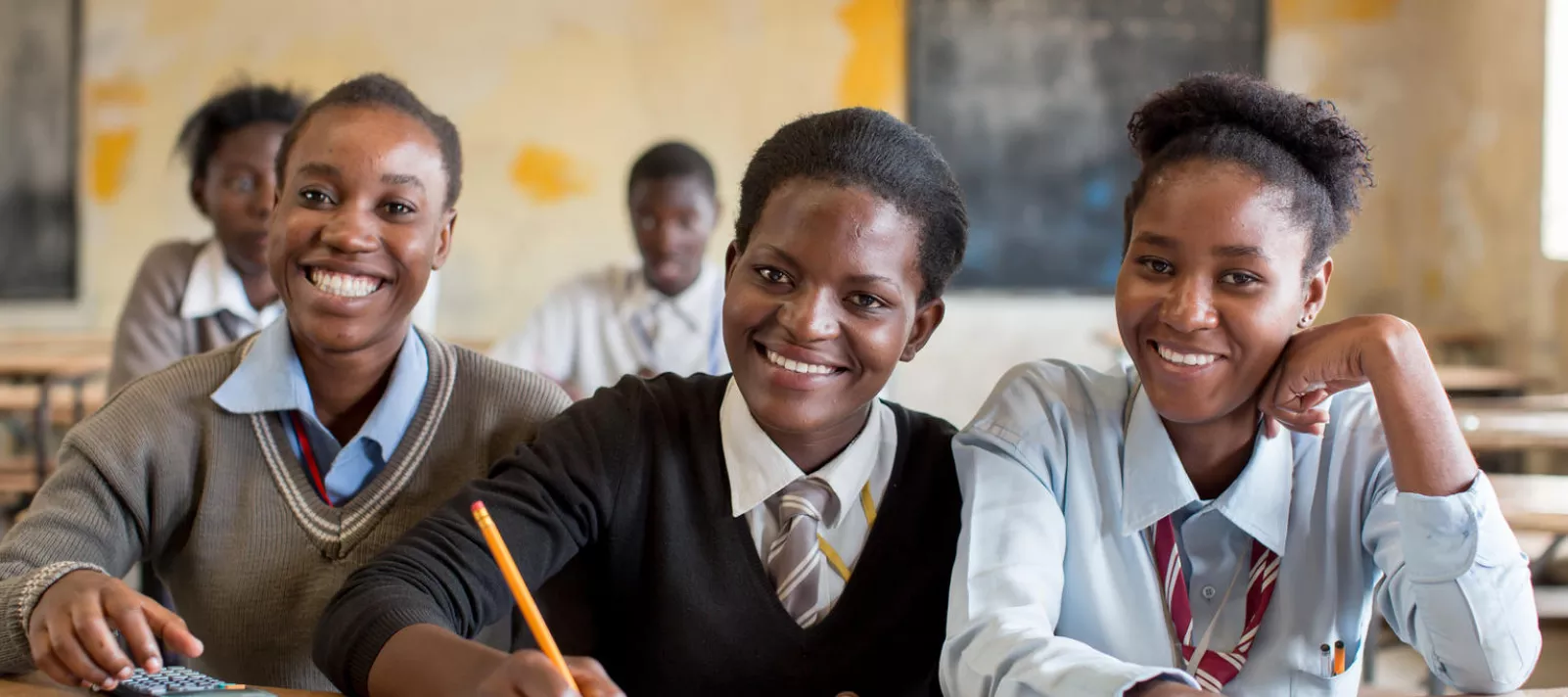 Adolescent girls, including one taking notes, smile during a class