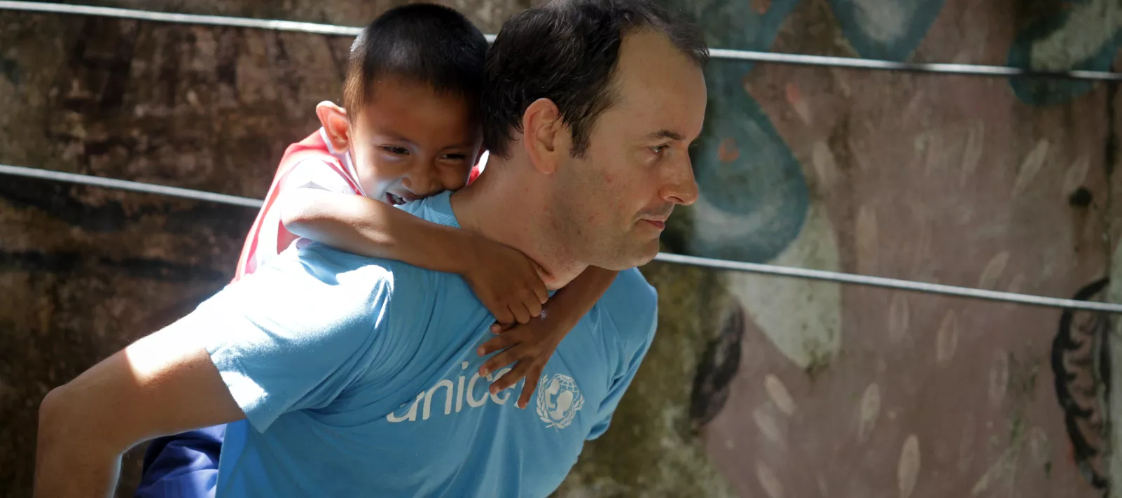 A male UNICEF officer is piggybacking a young boy.