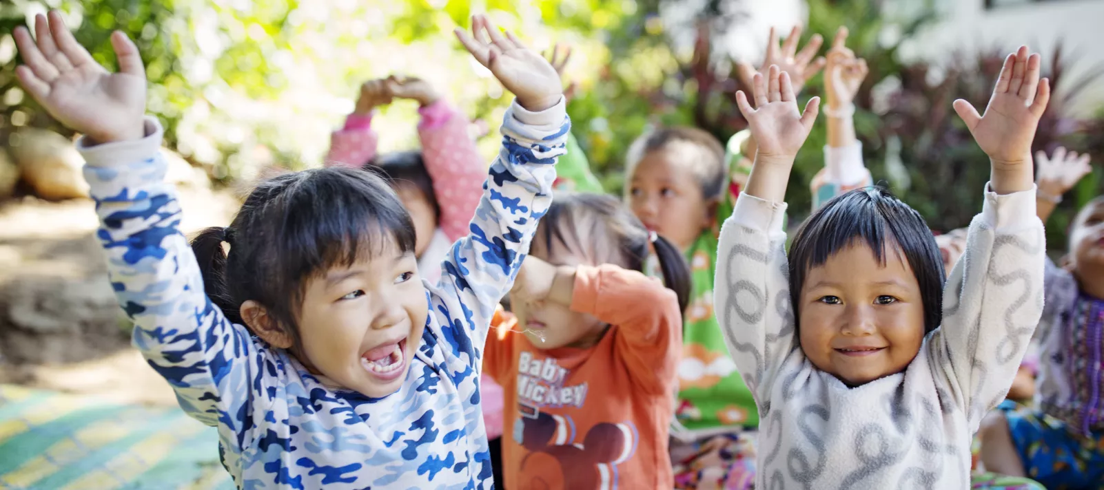 A group of young children are happily raising their hands.