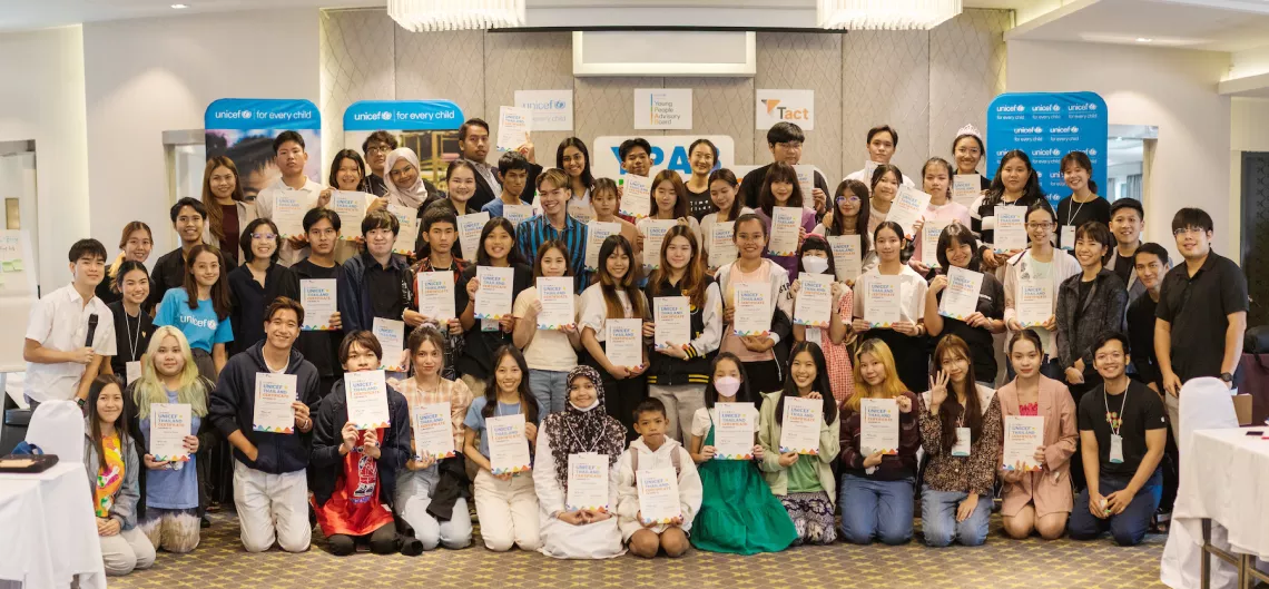 A group of young people holding certificates and smiling in a conference room with UNICEF banners in the background.