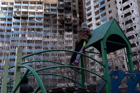 Дівчинка на дитячому майданчику біля багатоквартирного будинку в Києві, обстріляного вранці 7 лютого 2024 року, дивиться на випалені квартири.