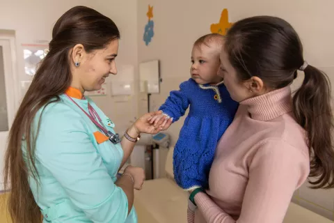Hanna, the mother of seven-month-old Mariyka holds her daughter in her arms. The girl is holding the hand of the nurse to whom she came for a medical examination.