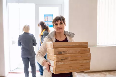 Жінка тримає в руках 5 картонних коробок із лептопами