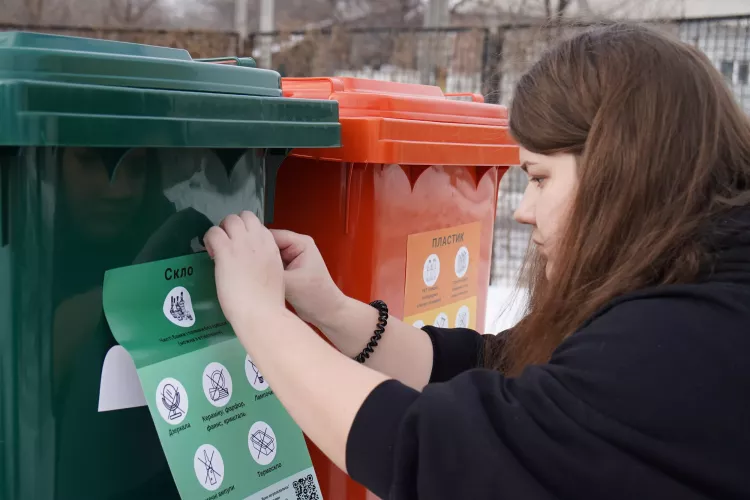 Oleksandra, a member of the "Clean Environment" team, glues stickers on containers that indicate how to sort waste properly 