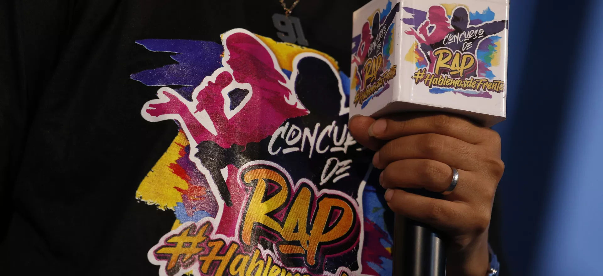animador del evento de premiación del concurso de rap Hablemos de frente sostiene micrófono mostrando el logotema del concurso