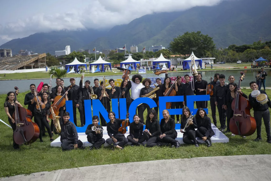 Niños, niñas y adolescentes músicos integrantes de la orquesta Caracas Big Band se toman foto con letras que dicen UNICEF