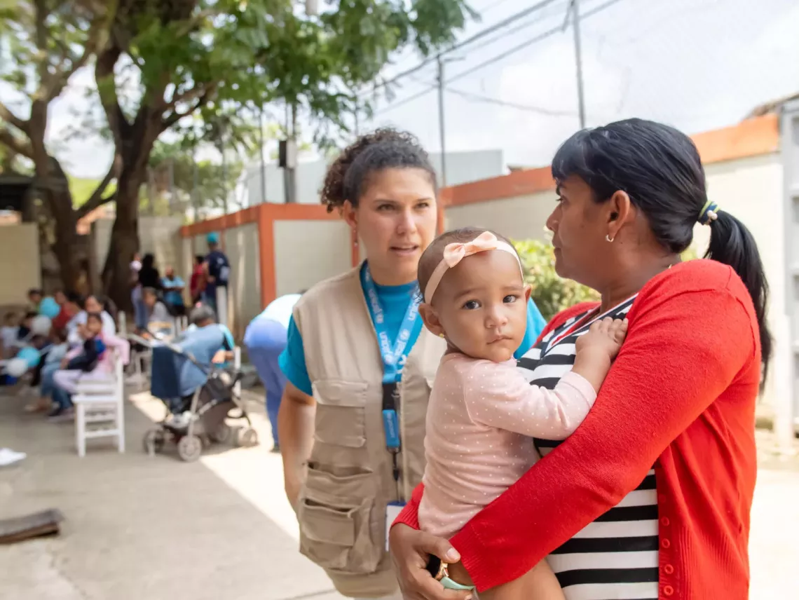 Yelitza Grimán, maestra de escuela, carga a su sobrina mientras conversa con Verónica Castillo, personal de UNICEF, durante una jornada de atención integral apoyada por UNICEF en Las Tejerías, estado Aragua, el 18 de mayo de 2023.