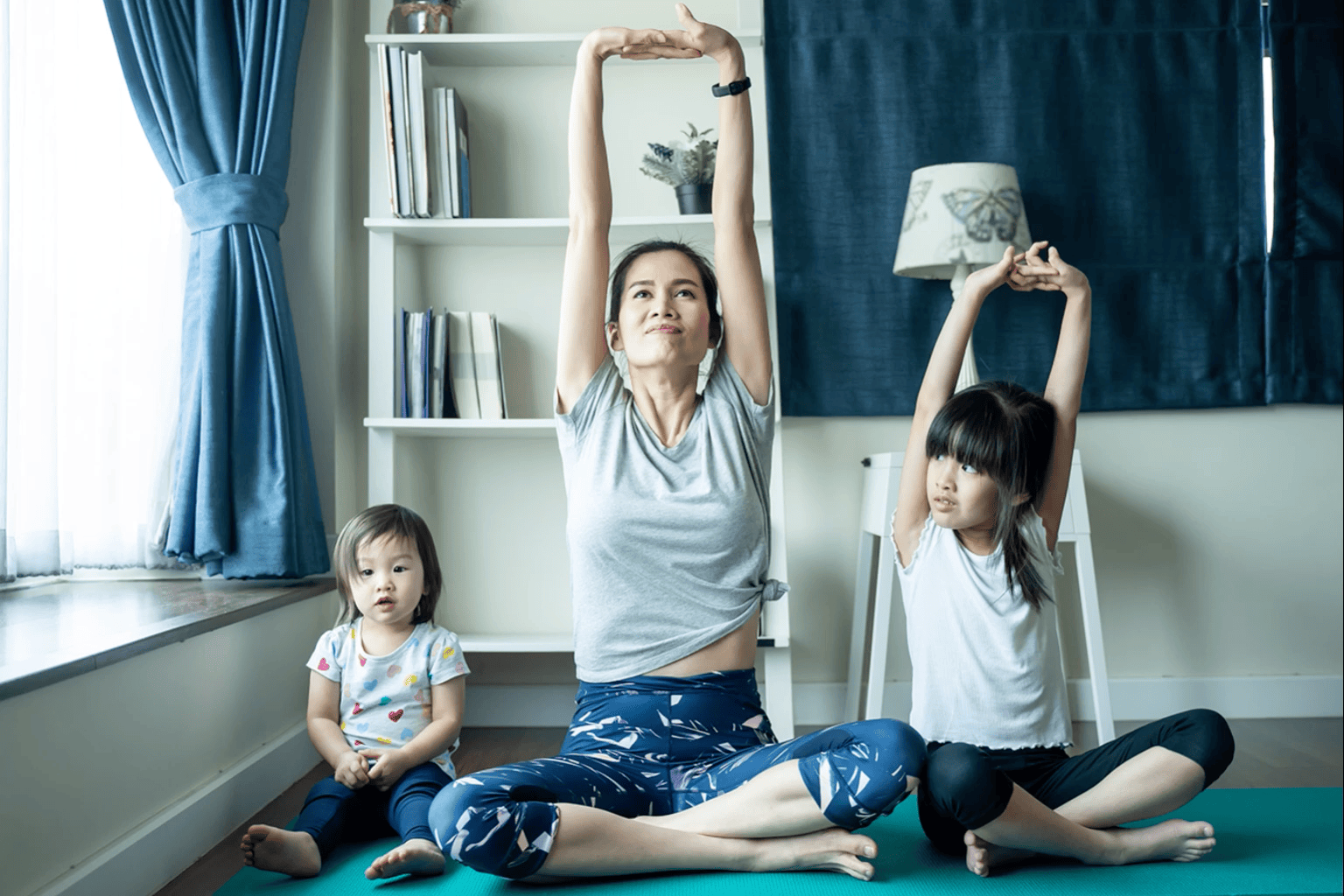 A mother and her two children sitting together on the floor and stretching. 