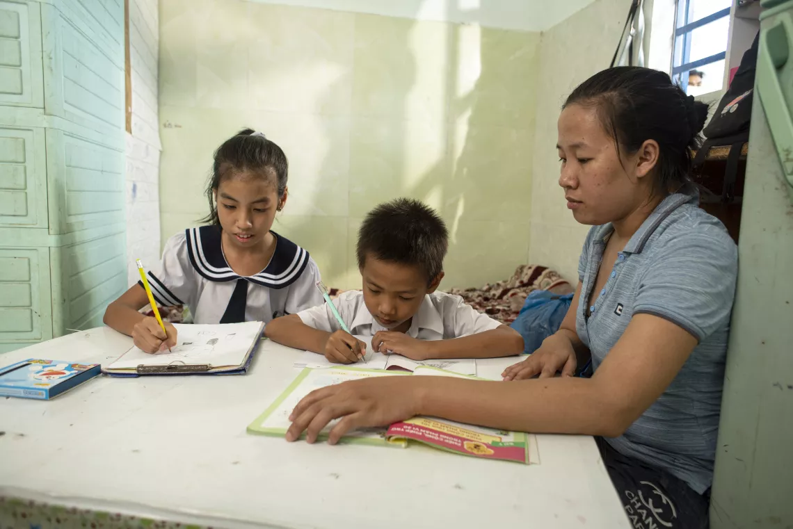 Chị Ngô Thị Phương giúp hai con nhỏ của mình làm bài tập về nhà. Gia đình chị Phương được nhận hỗ trợ tiền mặt từ Chương trình Bảo trợ Xã hội tại TP Đà Nẵng.