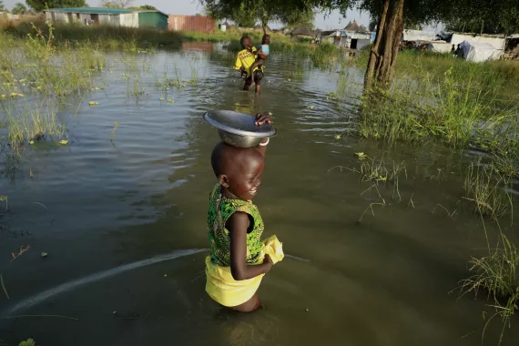 A young girl in the floodwater, carrying a utensil as she follows her siblings in Panyagor of Twic East of Jonglei state.