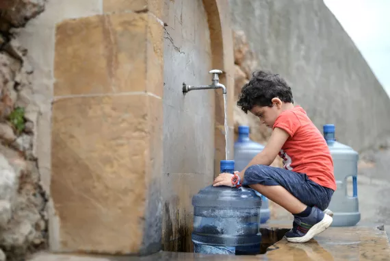 Georgio is helping his parents fill their small water containers because they don't have water at home.