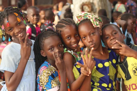 A group of children standing, smiling and doing the "peace sign" with their hands