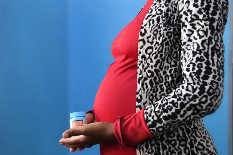 Close-up on a pregnant woman's belly and her hands holding her HIV treatment