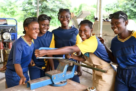 Five adolescent girls smiling as they undertake vocational training on metalwork.
