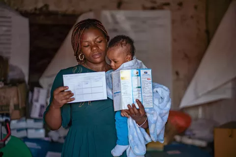A mother holding her baby and his vaccination card