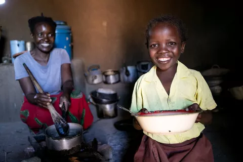 A school girl happily helps her mother prepare food in the kitchen