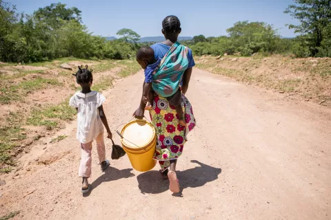 A mother walking with her children while carrying a bucket.