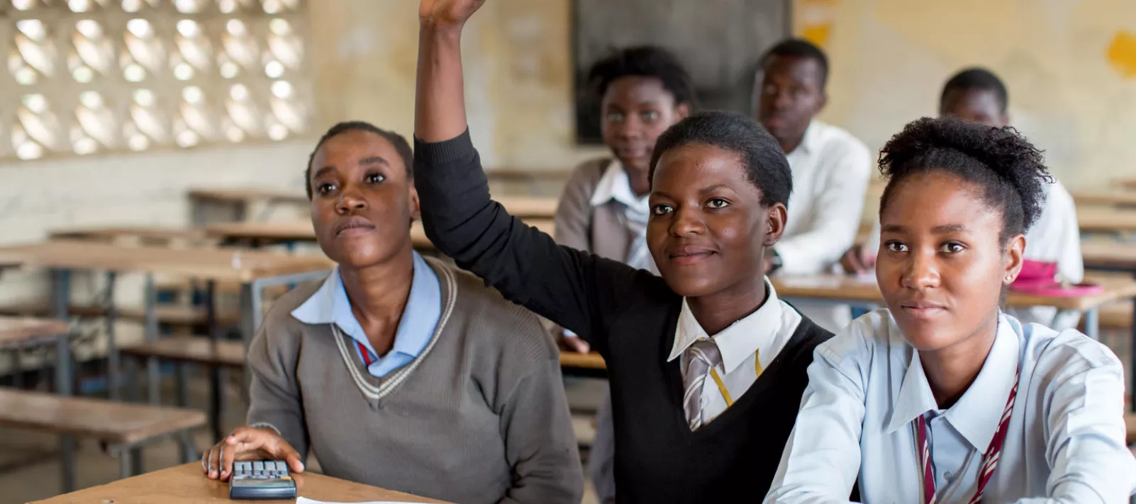 An adolescent school girl raises her hand in a classroom in Lusaka, Zambia