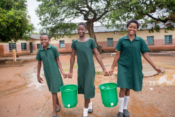 Students carry buckets filled with water and on which taps have been installed