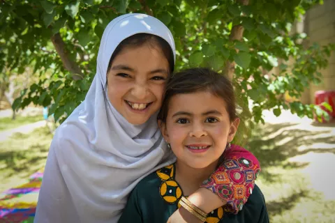 In May 2022, two young girls smiling outside of a health and nutrition clinic in Ghazni Province, Afghanistan.