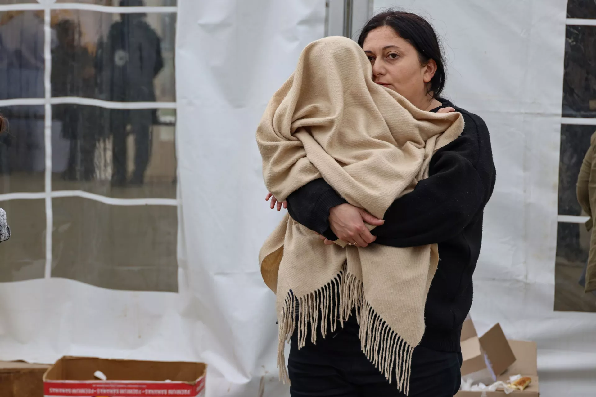 A refugee mother holding her child covered in a blanket in her arms
