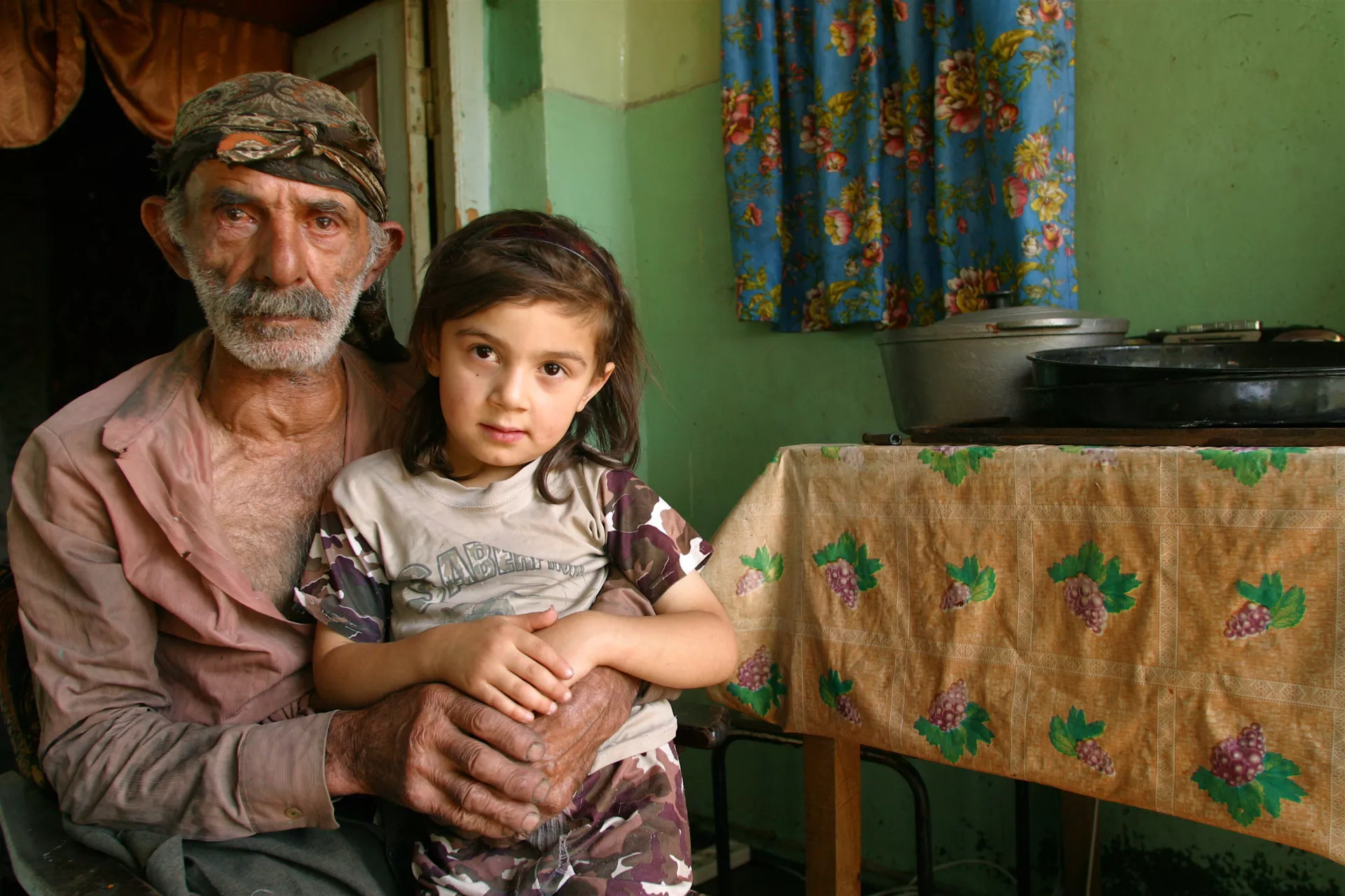A girl stands by her father at their home.