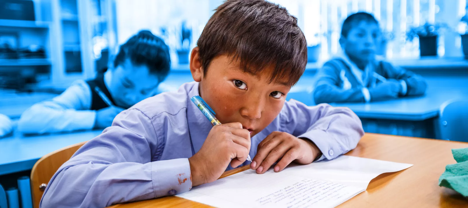 A boy looks the camera as he diligently writes down notes during class in Mongolia
