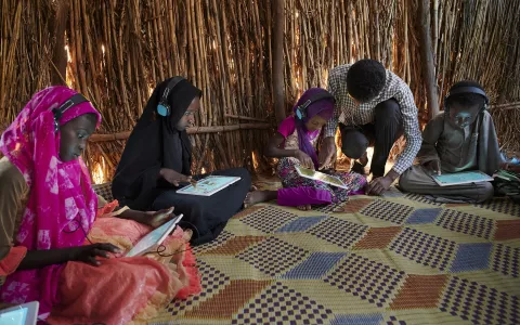 Sitting next to a girl child, a teacher, assists a girl child with her tablet, at the UNICEF supported Debate e-Learning Centre in a village in Sudan.