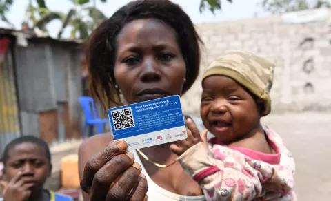 A woman, who is holding a baby, holds up a card