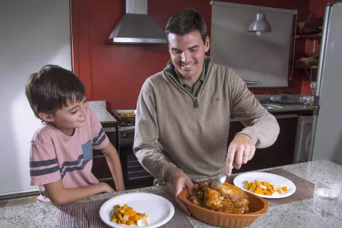 Un adulto y un niño, en una cocina, preparan alimentos juntos mientras sonríen