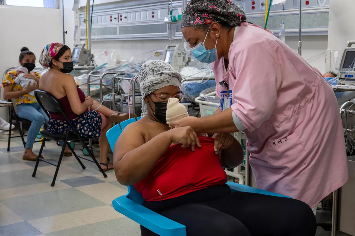 enfermera está ayudando a una madrea a cargar a su bebe recien nacido en el pecho, plan canguro