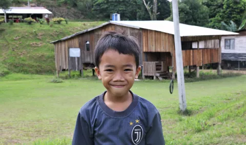 A boy smiling in front of a wooden house