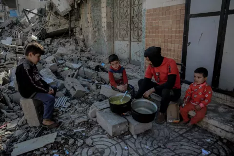Gaza Strip. A family cook a meal outside near piles of rubble from destroyed buildings.