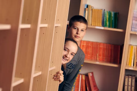 Dvoje djece vire iza police s knjigama