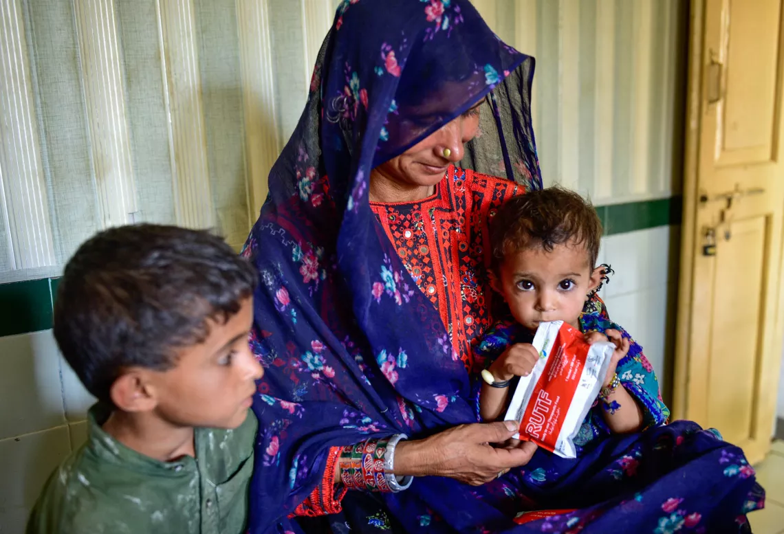 Mother with her two children as one tries to bite a packet of ready to use therapeutic food for malnourished children