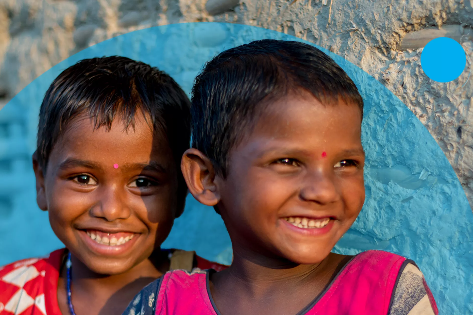 Two young children smile against a plaster wall, with blue polka dots and a 'World Children's Day 2019" logo added to the image.