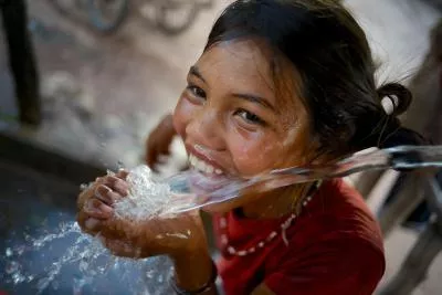 Una niña se ríe mientras bebe agua en un punto de agua en la aldea de Adone del distrito de Ta Oi, provincia de Saravane, RDP de Laos. 
