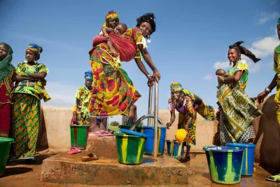 In late July 2015 in the Niger, with one of her two children in a sling on her back, Ramata, who is a member of the Fulani ethnic group, pumps water from a borehole into buckets, in the village of Yanja, Tillabéri Region. 