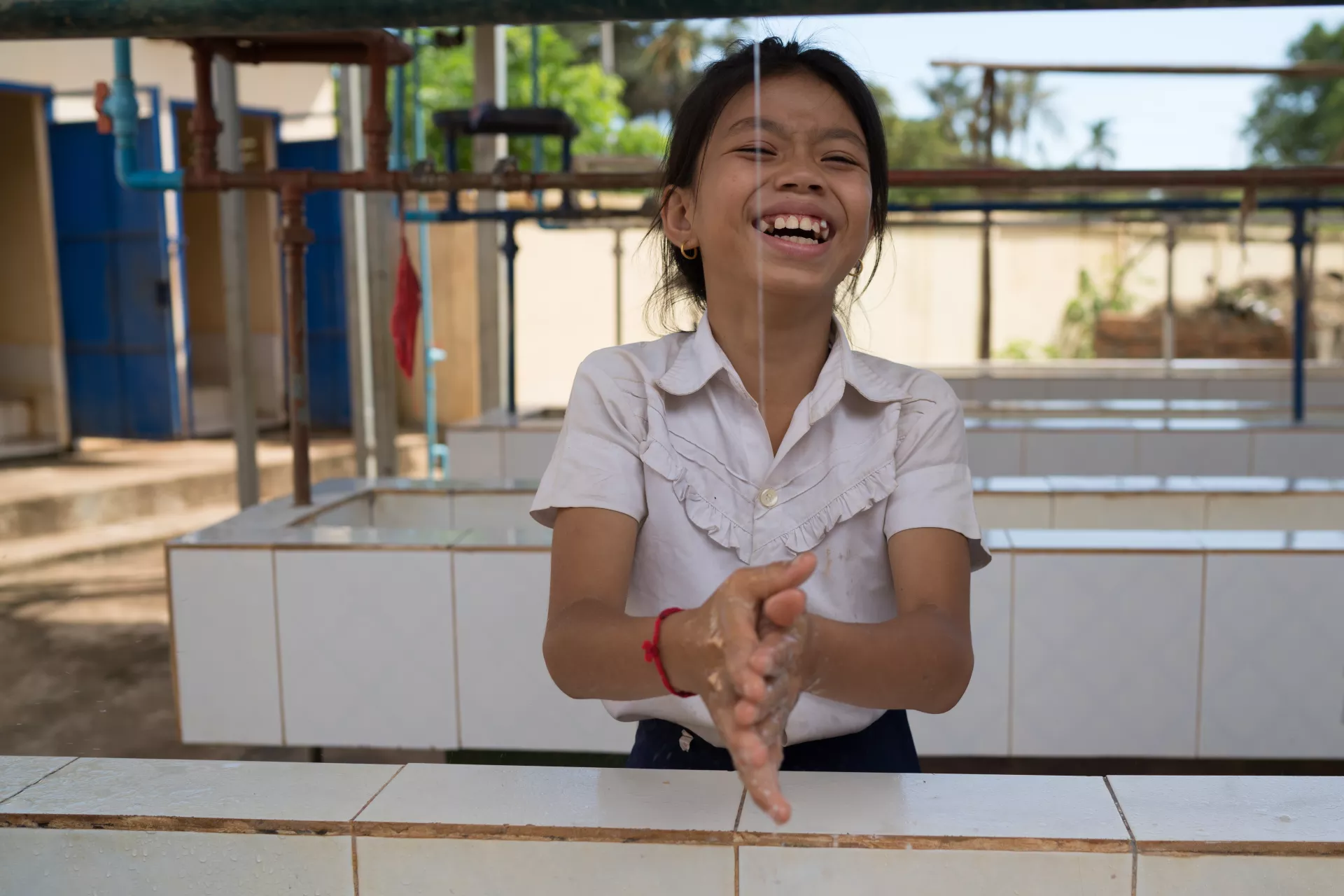تلميذة تبتسم وهي تغسل يديها عند مرفق المياه وخدمات الصرف الصحي والنظافة الصحية في مدرسة كامبونغ ثمار الابتدائية في قرية كانغ ساو.