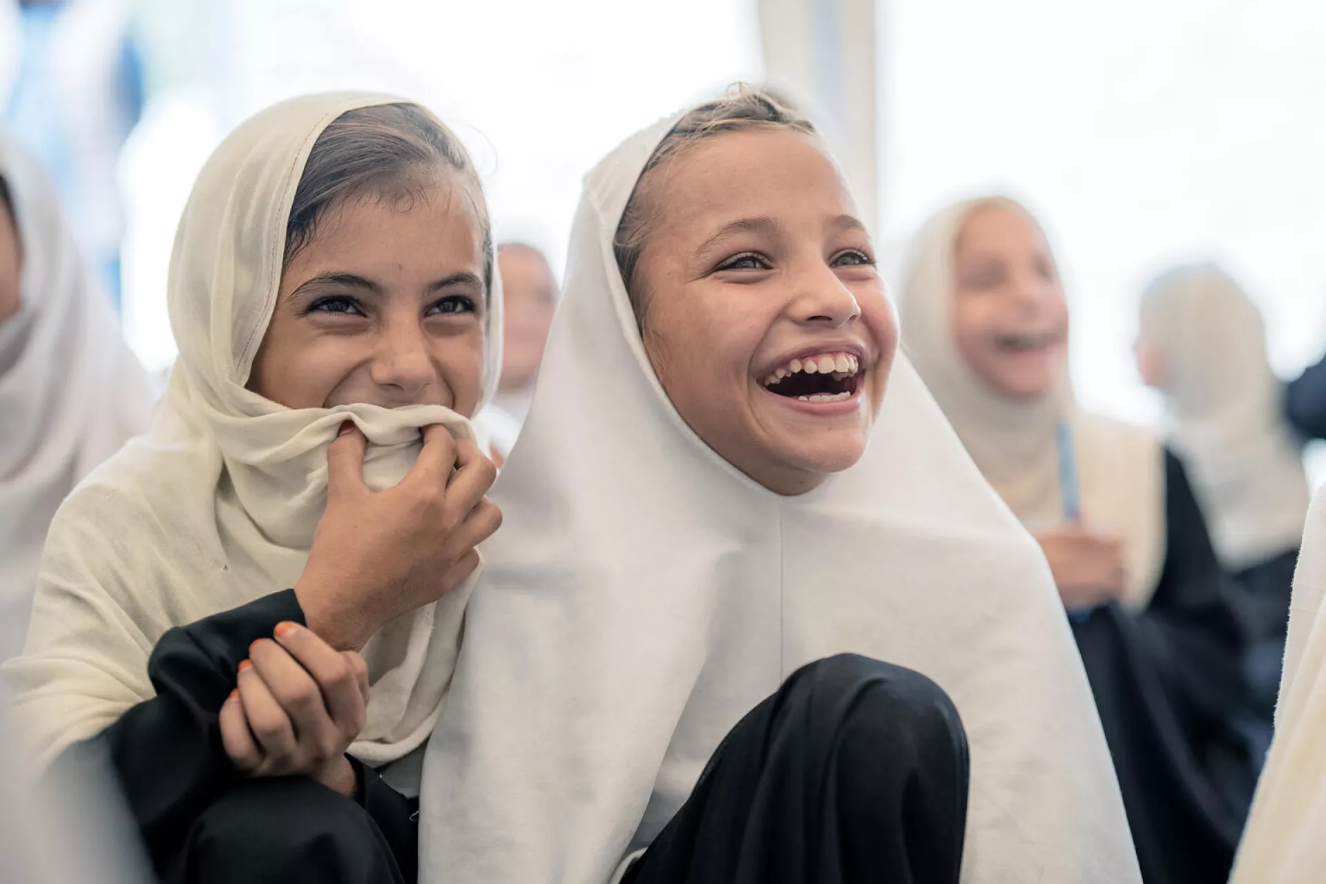 Two young girls smile all the way up to their eyes in a classroom in Afghanistan. Everything around them fades out.