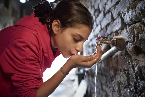 A girl drinks water from a tap