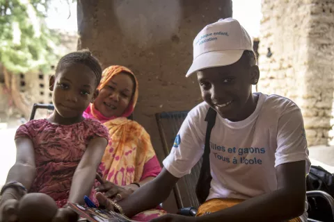 A girl in a UNICEF shirt smiles next to a mother and daughter, Mali